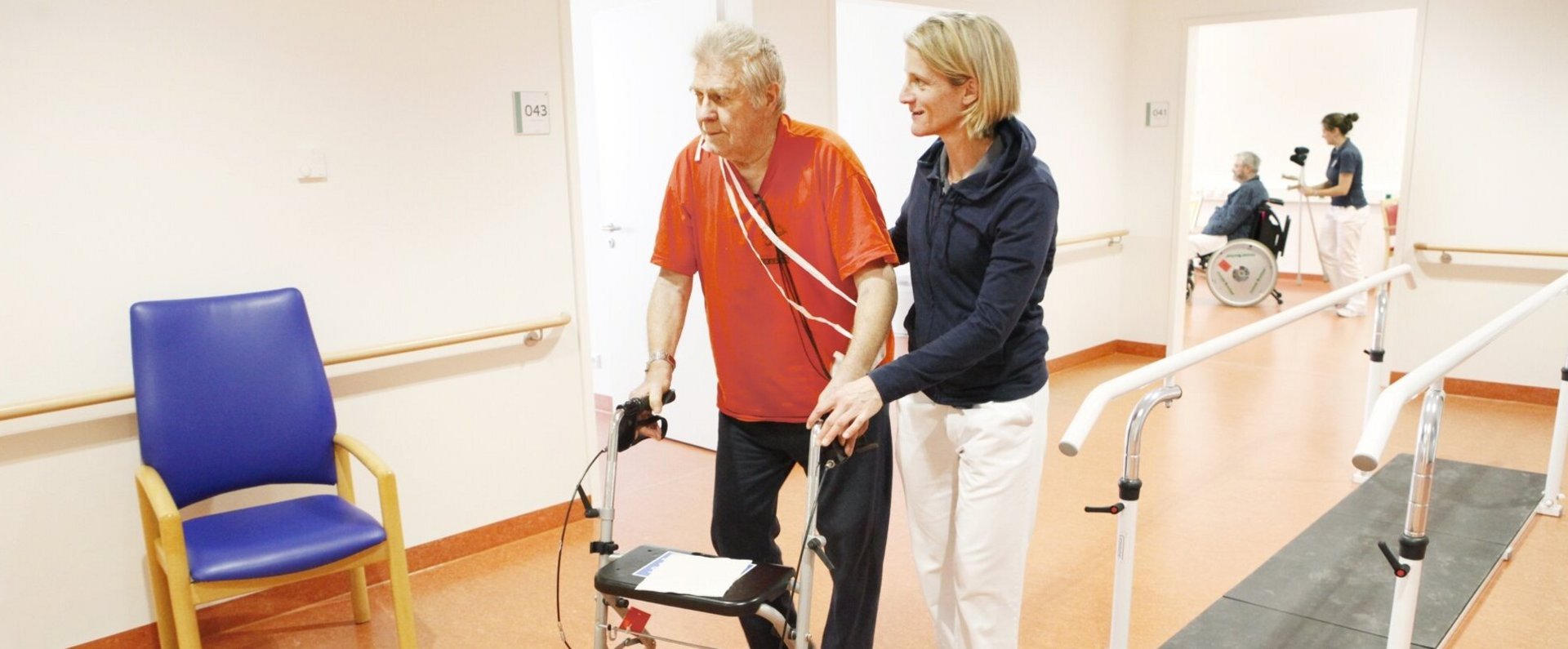 Physiotherapeutin unterstützt und begleitet Patienten beim Gehen mit Rollator.