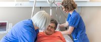 Zwei Pflegefachfrauen am Bett einer Patientin.