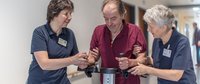 Zwei Physiotherapeutinnen unterstützen Patienten am Gehwagen.