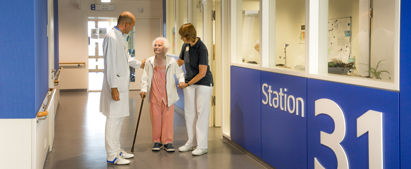 Arzt und Physiotherapeutin mit Patientin im Gang der Station 31. 
